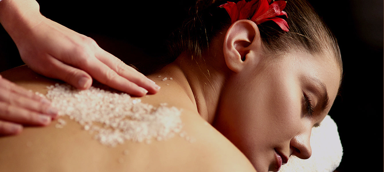 Person receiving a back massage with salt on the skin, wearing a red flower in their hair.