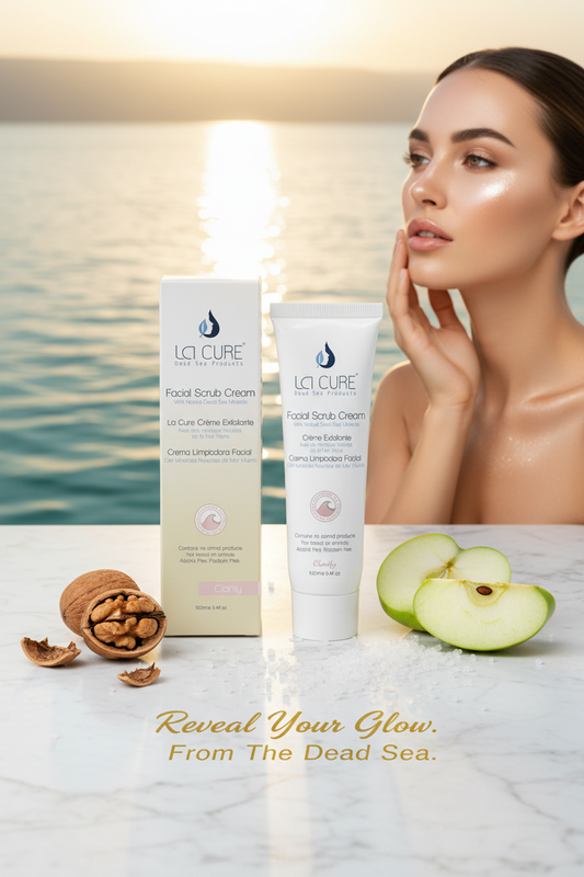 La Cure Facial Scrub Cream tube and box with walnut shell and apple extract beside the Dead Sea at golden hour for radiant glowing skin